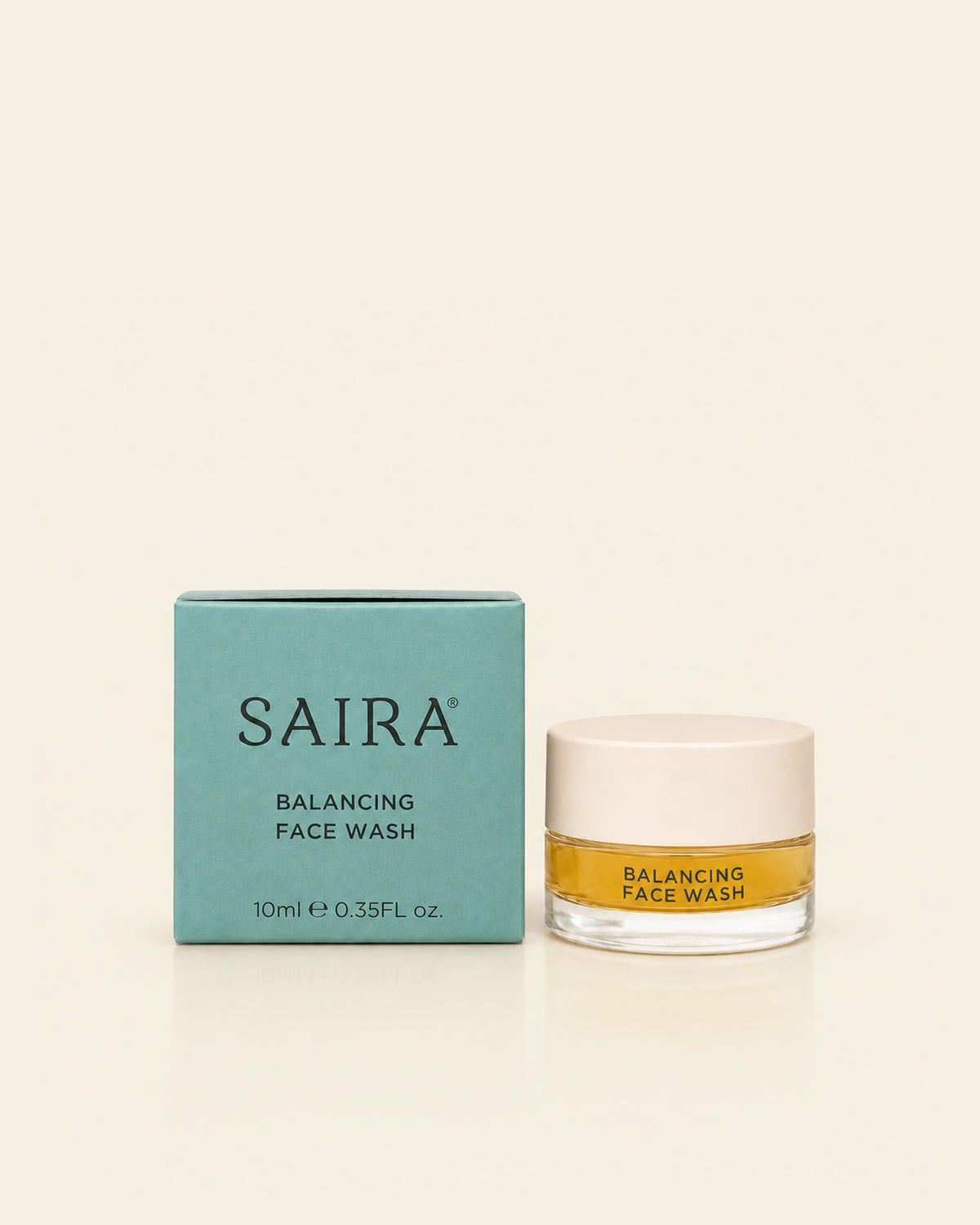 SAIRA Balancing Face Wash shown with its teal outer box and a clear glass jar containing golden-yellow liquid, set against a solid cream background.