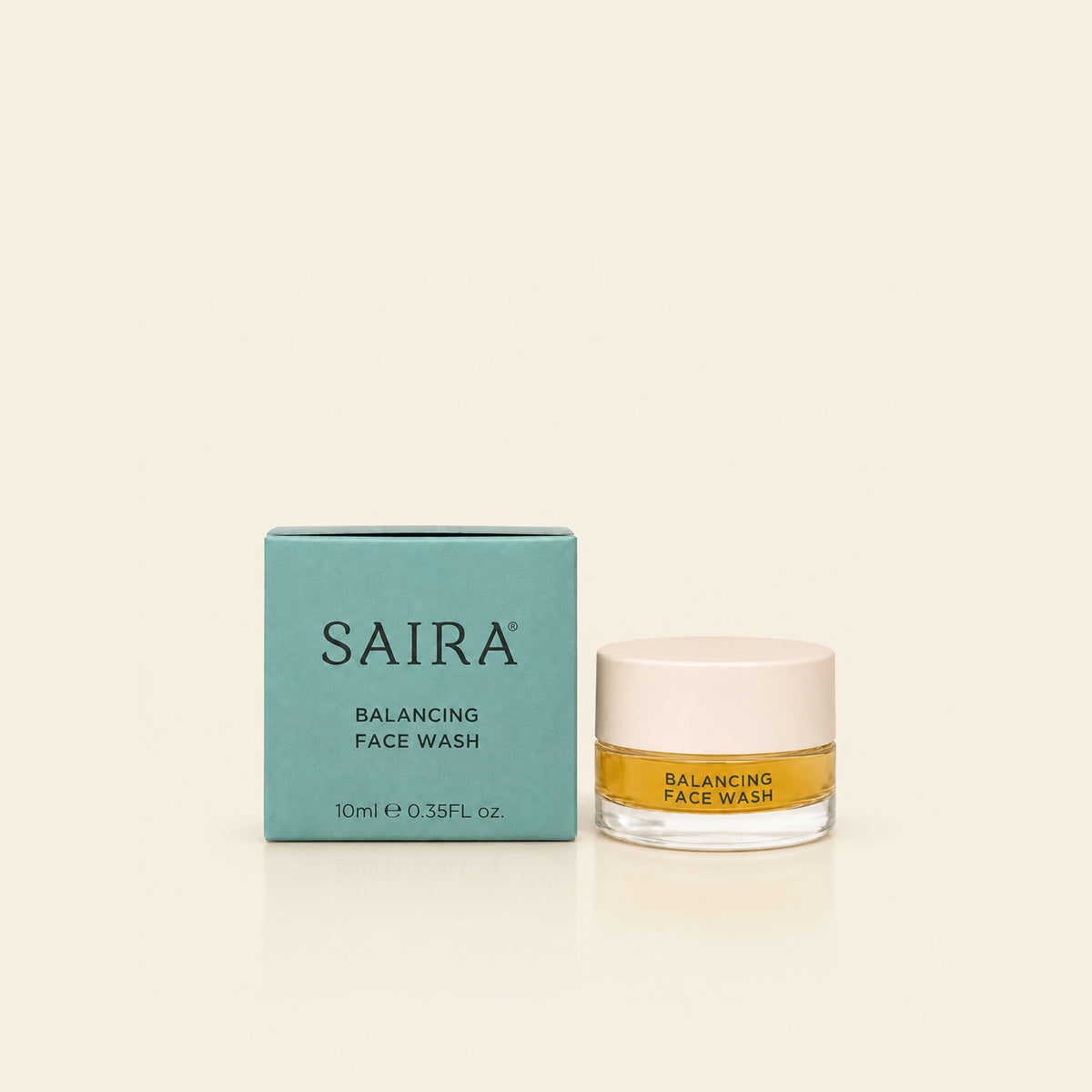 SAIRA Balancing Face Wash shown with its teal outer box and a clear glass jar containing golden-yellow liquid, set against a solid cream background.