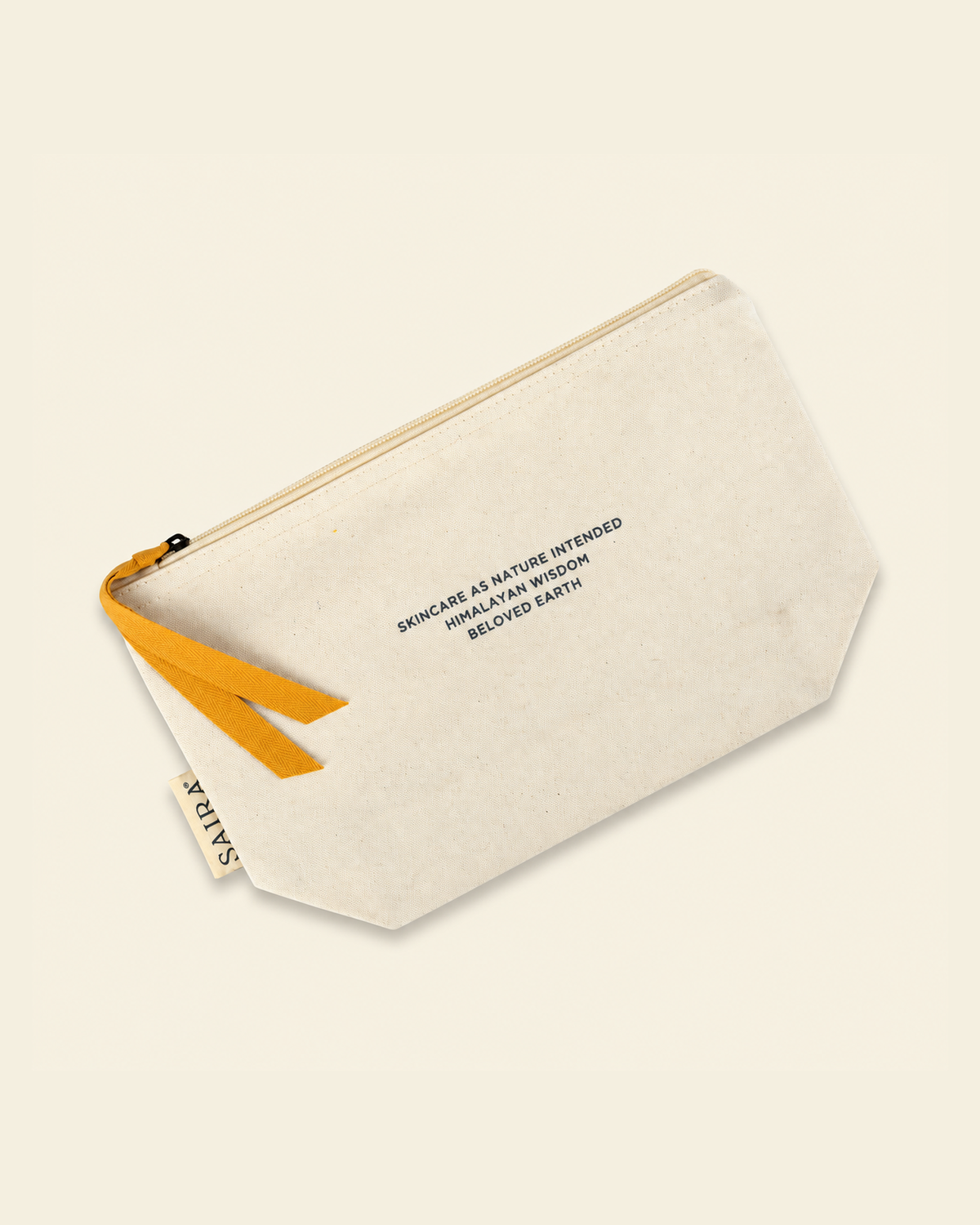 An off-white canvas pouch with a mustard yellow zipper pull and black printed text, shown on a solid cream background.