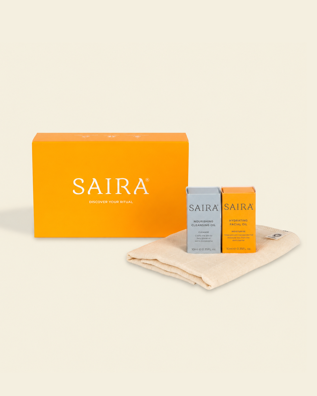 SAIRA skincare gift set featuring a large orange box, a gray bottle, and an orange bottle resting on a beige cotton cloth against a warm cream background.