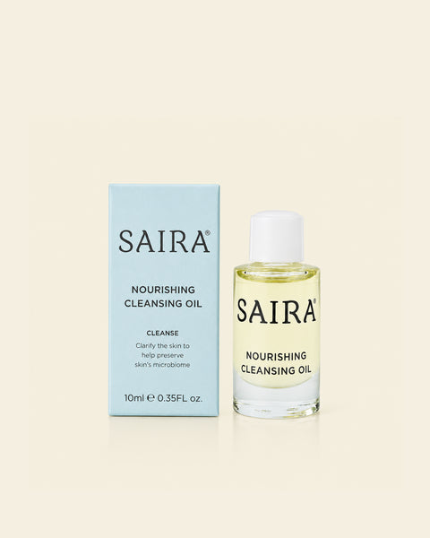 SAIRA Nourishing Cleansing Oil shown with its light blue outer box and the clear glass bottle containing pale yellow oil, set against a solid cream background.