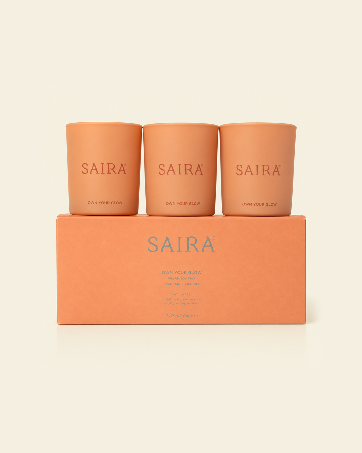 Three Saira candles in terracotta-colored glass jars sit on top of a matching rectangular box. The brand name 'SAIRA' is printed in a reddish-brown color on each jar and in a larger light blue-gray font on the box.