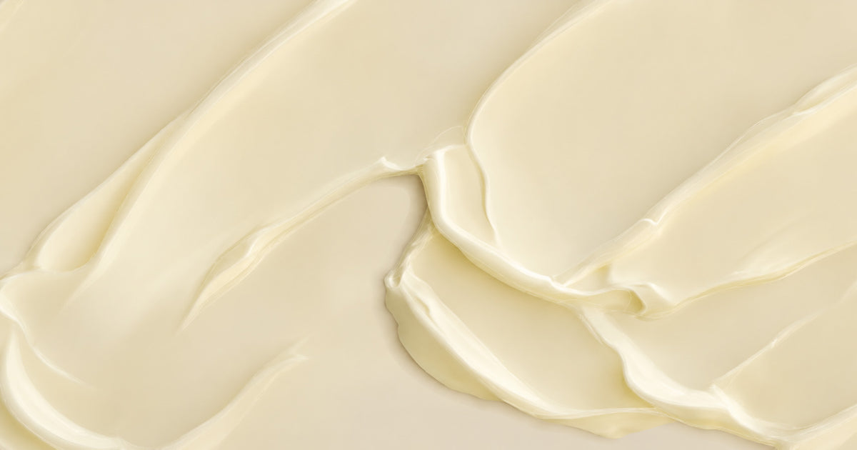 A close-up texture shot of a thick, creamy off-white cosmetic cream or lotion swirled across the frame.