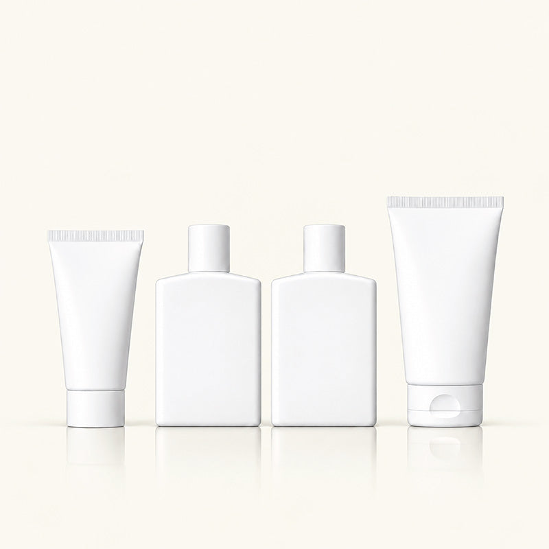 Four blank white cosmetic containers on a light cream background: two squeeze tubes and two rectangular bottles with caps, arranged symmetrically with soft reflections below.