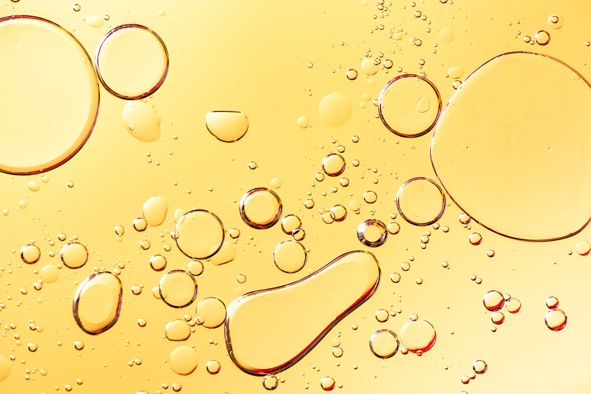 Close-up of a translucent golden yellow liquid with floating clear bubbles and droplets on a glossy surface.