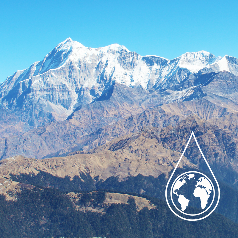 Snow-capped mountain peaks rise under a clear blue sky, with layered brown and dark forested hills in the foreground and a white teardrop-shaped globe icon overlaid near the lower right.